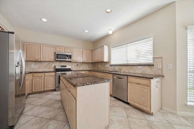 kitchen featuring appliances with stainless steel finishes, backsplash, light brown cabinetry, sink, and a kitchen island