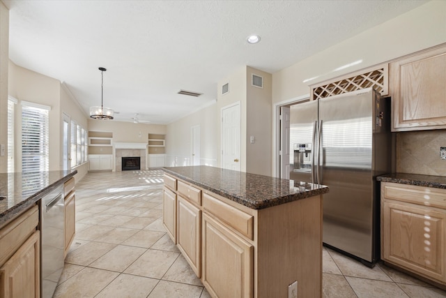 kitchen with hanging light fixtures, light tile patterned floors, a tiled fireplace, a kitchen island, and appliances with stainless steel finishes