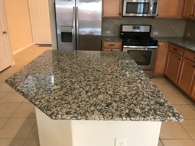 kitchen with backsplash, light tile patterned floors, stainless steel appliances, and dark stone counters