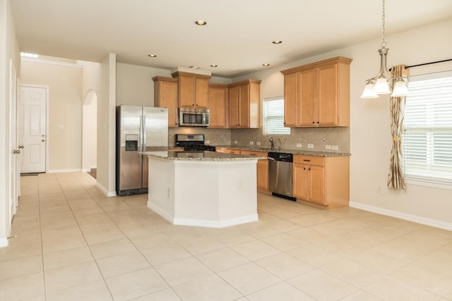 kitchen featuring light stone countertops, appliances with stainless steel finishes, decorative backsplash, decorative light fixtures, and a center island