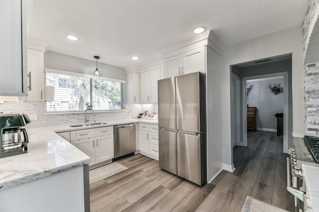 kitchen with sink, appliances with stainless steel finishes, decorative light fixtures, light hardwood / wood-style floors, and white cabinetry