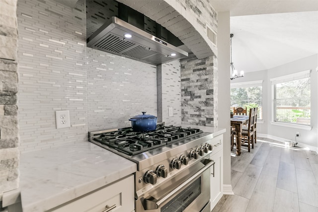 kitchen with white cabinets, high end stainless steel range, wall chimney exhaust hood, light wood-type flooring, and light stone countertops