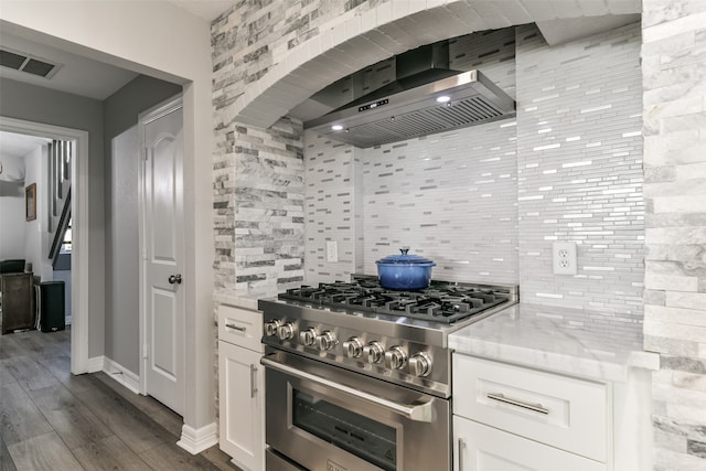 kitchen with high end range, tasteful backsplash, light stone counters, wall chimney range hood, and white cabinetry