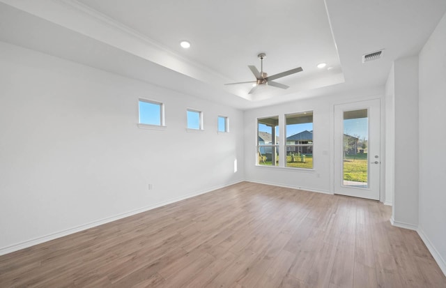 empty room with a tray ceiling, ceiling fan, and light hardwood / wood-style floors