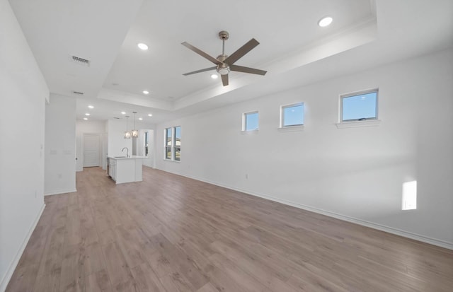 unfurnished living room with sink, light hardwood / wood-style flooring, and a tray ceiling