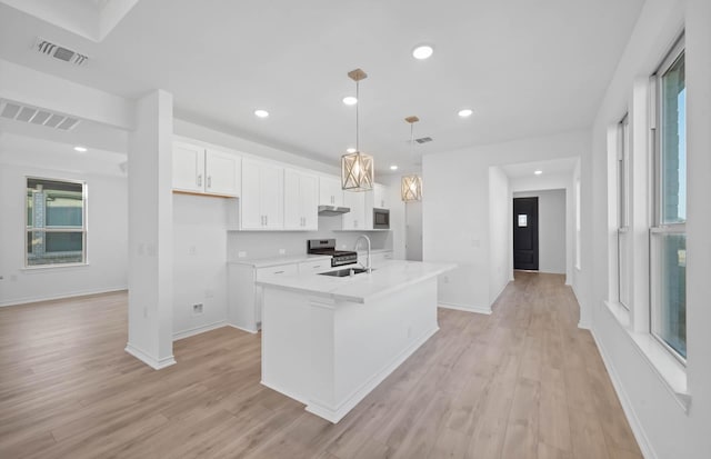 kitchen with light wood-type flooring, sink, decorative light fixtures, a center island with sink, and white cabinets