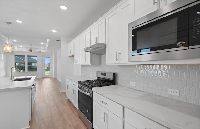 kitchen featuring light stone counters, stainless steel appliances, sink, white cabinetry, and hanging light fixtures