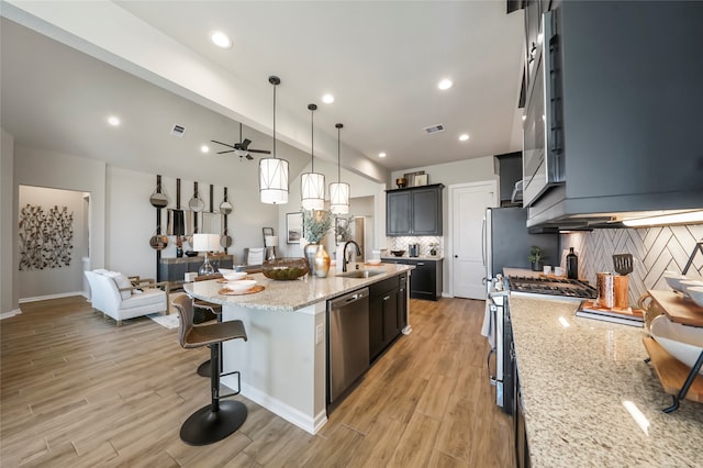 kitchen with ceiling fan, stainless steel appliances, decorative light fixtures, decorative backsplash, and a center island with sink