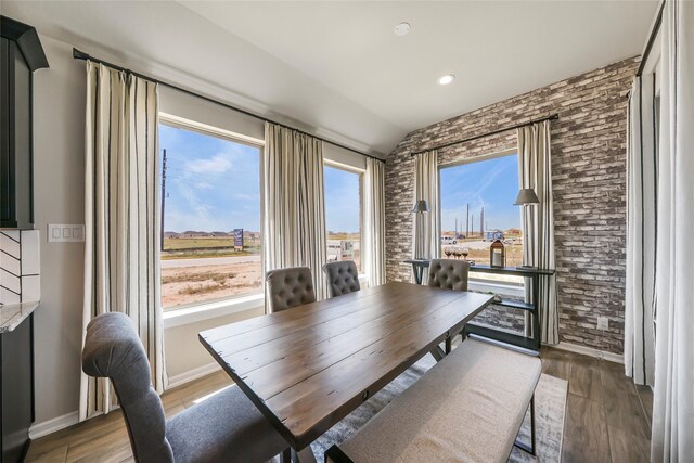 dining space featuring dark hardwood / wood-style floors, lofted ceiling, and brick wall