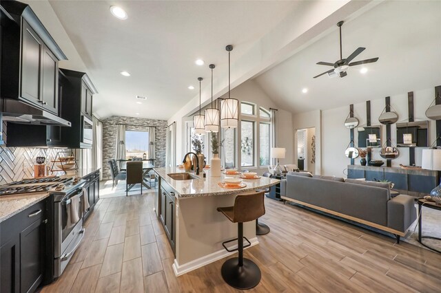 kitchen with a breakfast bar, stainless steel gas range oven, light stone counters, pendant lighting, and a center island with sink