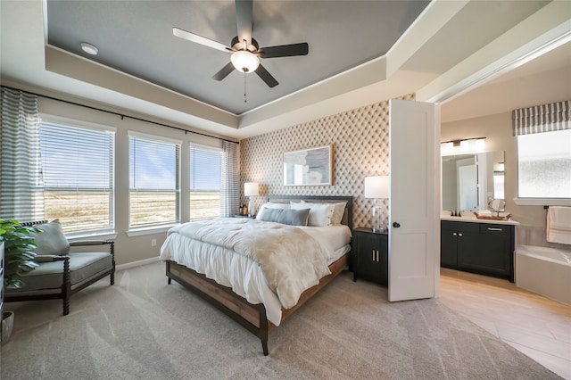 bedroom featuring a tray ceiling, connected bathroom, ceiling fan, and sink