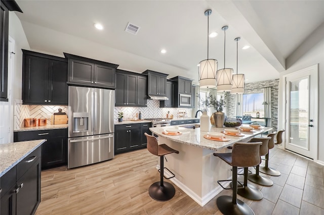 kitchen featuring light stone countertops, stainless steel appliances, pendant lighting, a breakfast bar, and a center island with sink