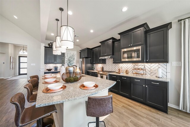 kitchen featuring lofted ceiling, a center island with sink, a kitchen breakfast bar, appliances with stainless steel finishes, and decorative light fixtures