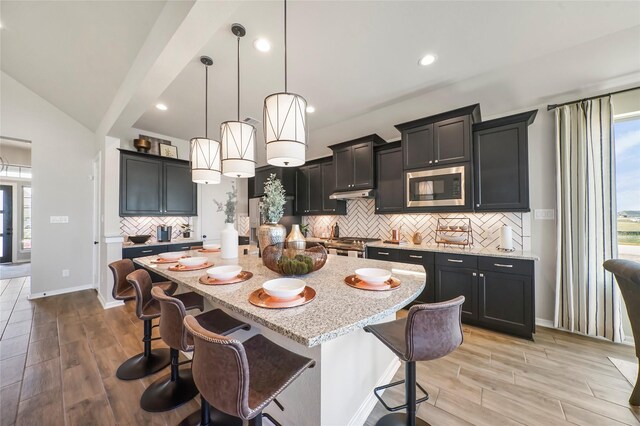 kitchen with light hardwood / wood-style floors, decorative light fixtures, a kitchen bar, a center island with sink, and appliances with stainless steel finishes