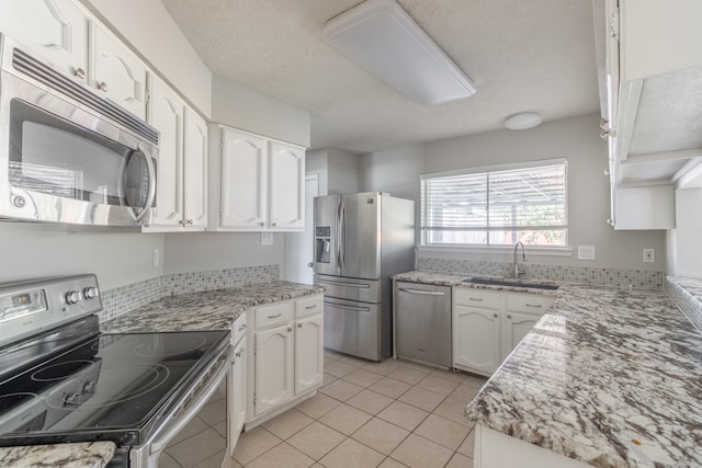 kitchen with white cabinets, sink, light tile patterned floors, a textured ceiling, and stainless steel appliances