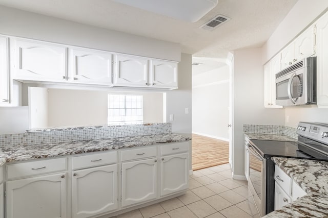 kitchen featuring white cabinetry, a textured ceiling, decorative backsplash, light tile patterned floors, and appliances with stainless steel finishes