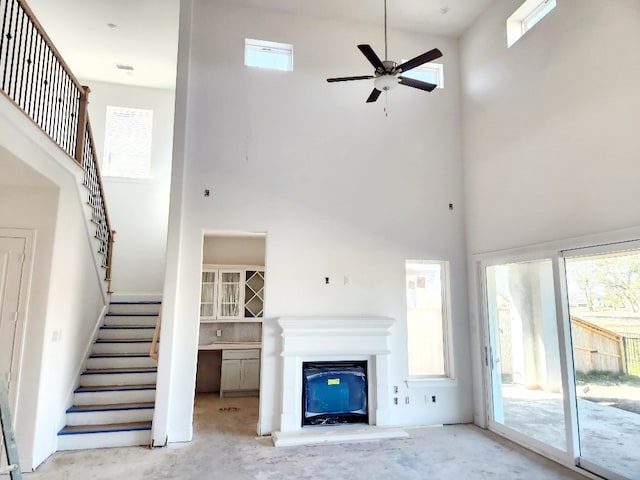 unfurnished living room with a high ceiling, concrete floors, ceiling fan, and a healthy amount of sunlight