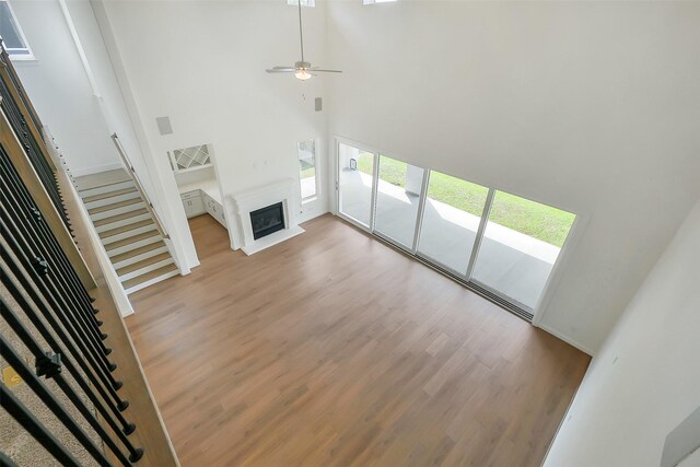 9923 Hunters Run Dr, Missouri City, TX 77459 - unfurnished living room with light wood-style floors, stairway, a high ceiling, a glass covered fireplace, and a ceiling fan