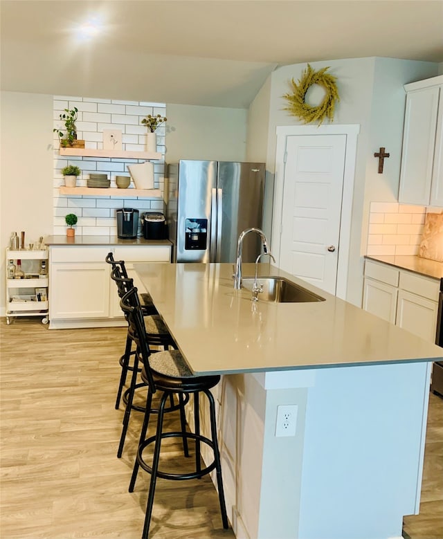 kitchen with white cabinets, stainless steel fridge, sink, and an island with sink