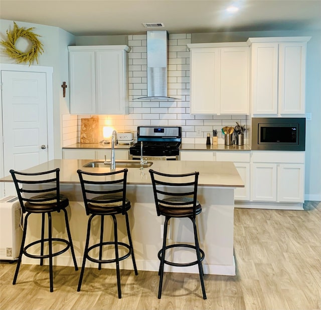 kitchen with white cabinetry, stainless steel microwave, wall chimney range hood, range with gas cooktop, and light hardwood / wood-style floors