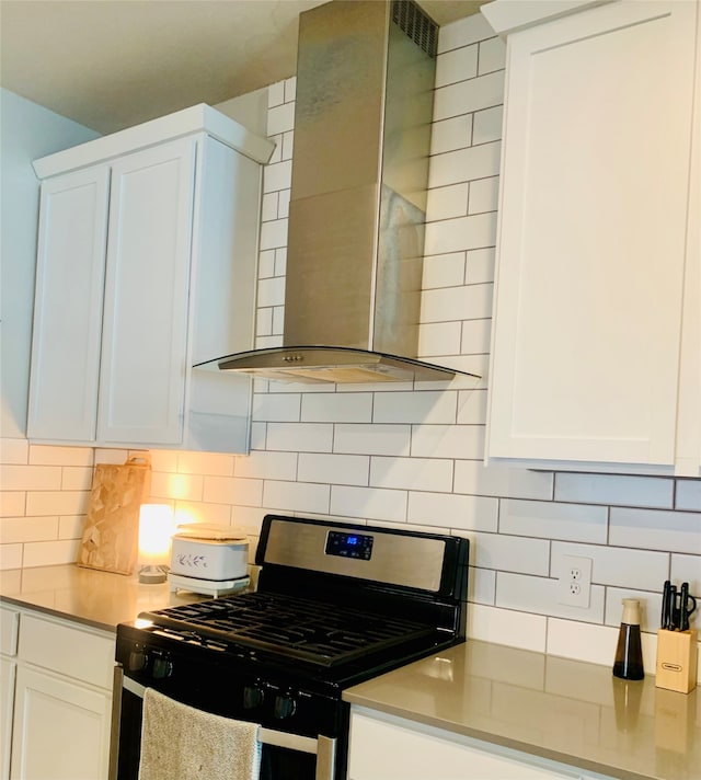 kitchen featuring white cabinets, gas stove, wall chimney range hood, and backsplash