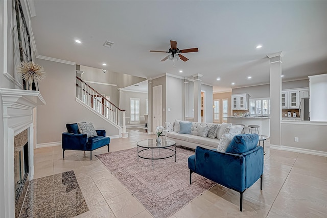 tiled living room with ceiling fan, a tile fireplace, crown molding, and a wealth of natural light