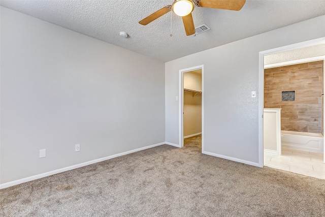 unfurnished bedroom featuring a textured ceiling, a walk in closet, light colored carpet, and ceiling fan