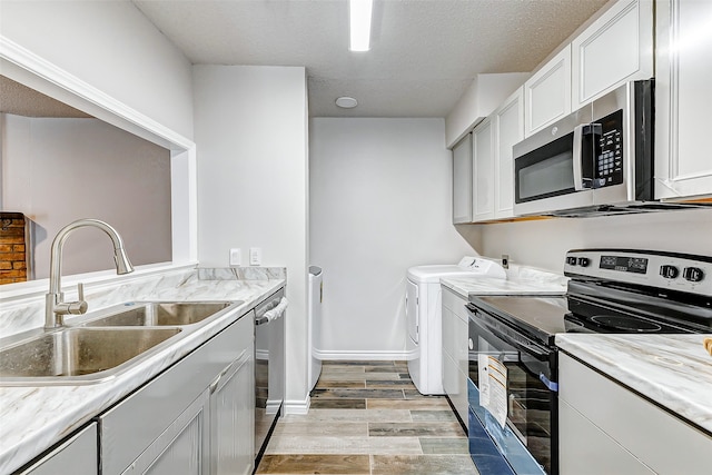 kitchen with appliances with stainless steel finishes, washer and clothes dryer, sink, light hardwood / wood-style floors, and white cabinetry