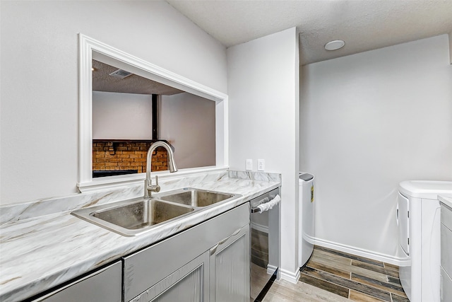 kitchen with sink, light hardwood / wood-style flooring, stainless steel dishwasher, independent washer and dryer, and a textured ceiling