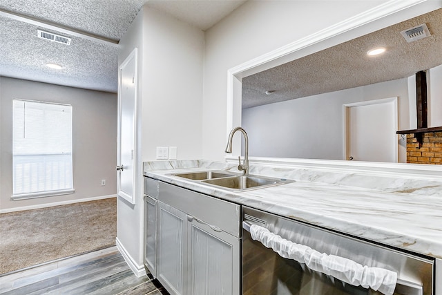 kitchen with a textured ceiling, light hardwood / wood-style floors, stainless steel dishwasher, and sink