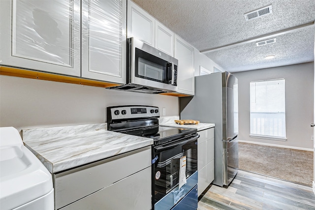 kitchen featuring a textured ceiling, stainless steel appliances, light hardwood / wood-style flooring, and white cabinetry