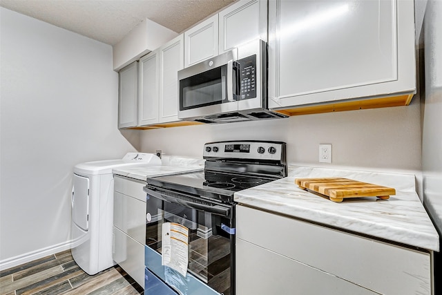 kitchen with stainless steel appliances, hardwood / wood-style floors, a textured ceiling, white cabinets, and washer and dryer