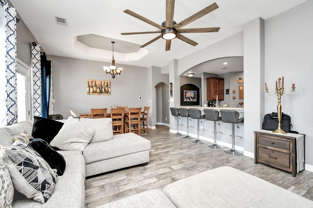 living room with a tray ceiling, light hardwood / wood-style flooring, and ceiling fan with notable chandelier