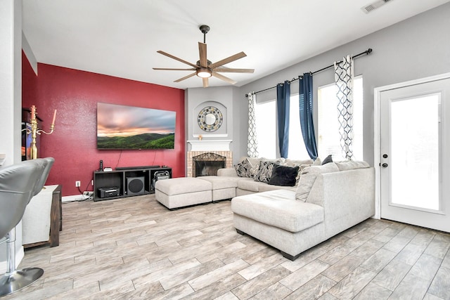 living room featuring ceiling fan, a healthy amount of sunlight, and a brick fireplace