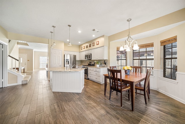 kitchen featuring stainless steel appliances, hanging light fixtures, dark wood-type flooring, and a kitchen island with sink