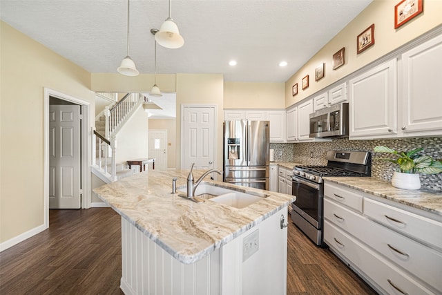 kitchen featuring stainless steel appliances, dark hardwood / wood-style floors, white cabinetry, hanging light fixtures, and an island with sink