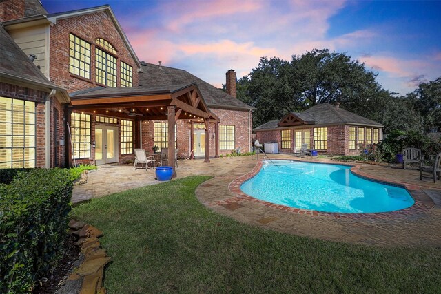 pool at dusk featuring french doors and a patio area