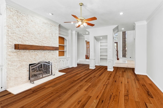 unfurnished living room featuring built in shelves, crown molding, hardwood / wood-style floors, and a fireplace