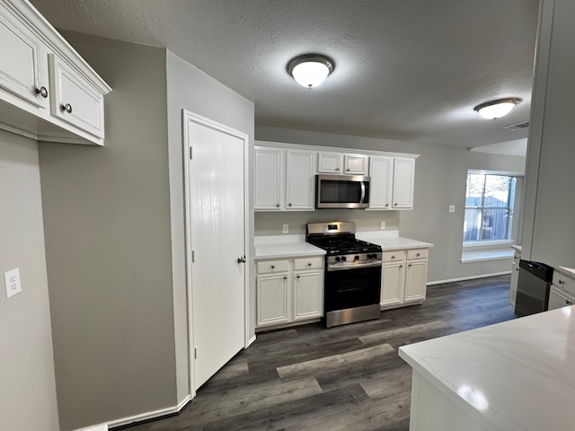 kitchen featuring dark wood-type flooring, white cabinets, light stone countertops, a textured ceiling, and appliances with stainless steel finishes