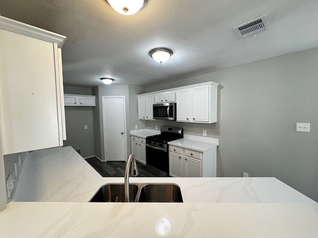 kitchen featuring sink, dark wood-type flooring, a textured ceiling, white cabinets, and appliances with stainless steel finishes