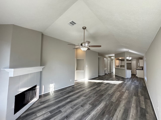 unfurnished living room with a tile fireplace, vaulted ceiling, dark hardwood / wood-style floors, ceiling fan, and a textured ceiling