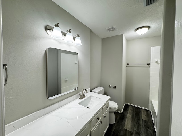 full bathroom with hardwood / wood-style floors, vanity, bathing tub / shower combination, toilet, and a textured ceiling