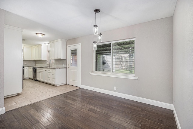 kitchen featuring backsplash, hanging light fixtures, stainless steel dishwasher, light wood-type flooring, and white cabinetry