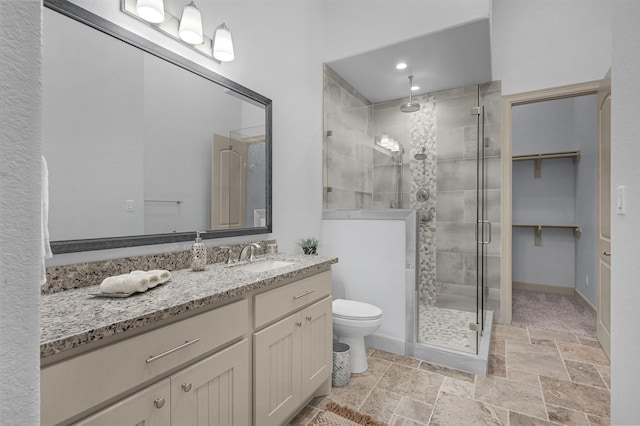 full bathroom featuring toilet, vanity, a shower stall, a walk in closet, and stone tile flooring