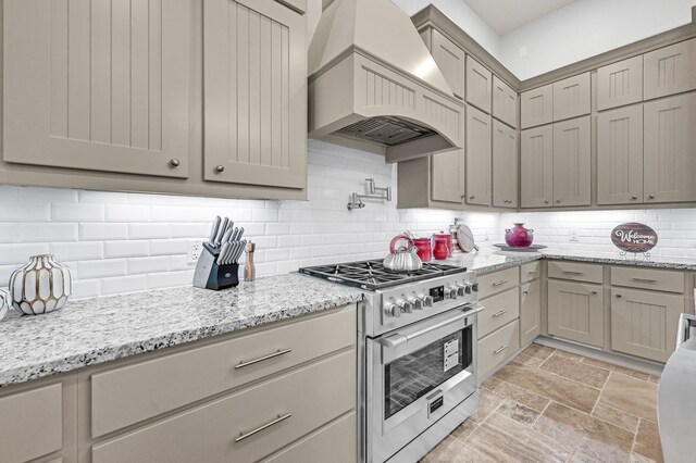 kitchen featuring decorative backsplash, light stone countertops, custom range hood, and high end stainless steel range oven