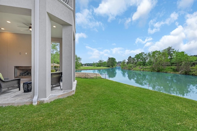 view of yard with ceiling fan, a patio, a water view, and a fireplace