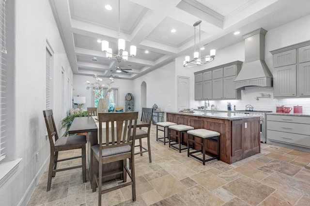 kitchen featuring a kitchen island with sink, stainless steel stove, a notable chandelier, and custom exhaust hood