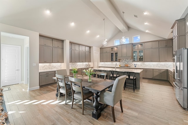 dining room featuring beam ceiling, light wood-type flooring, sink, and high vaulted ceiling