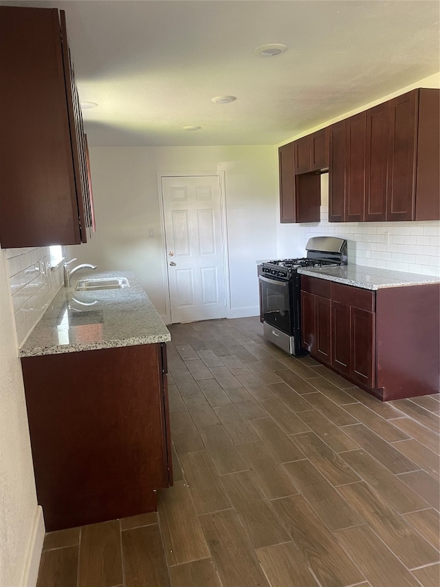 kitchen with gas range, light stone countertops, sink, dark hardwood / wood-style floors, and backsplash