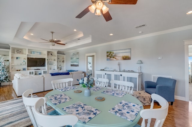 dining space featuring a raised ceiling, ceiling fan, light hardwood / wood-style flooring, and crown molding